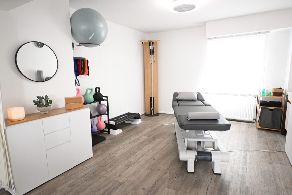 Heller Behandlungsraum der Physiotherapiepraxis Medica Artes in Köln mit moderner Behandlungsliege, Trainingsgeräten und funktioneller Ausstattung.