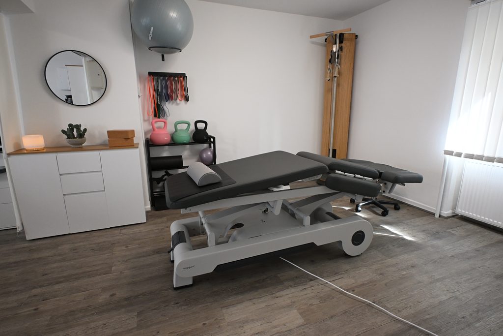 Moderner Behandlungsraum der Physiotherapiepraxis Medica Artes in Köln mit elektrisch verstellbarer Behandlungsliege und therapeutischen Trainingsgeräten.